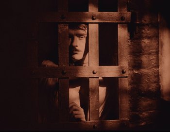 Movie still from “Intolerance” (1916), directed by D.W. Griffith – A man standing behind bars in a jail cell; Close Up shot, High angle