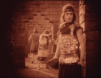 Movie still from “Intolerance” (1916), directed by D.W. Griffith – A man dressed as a roman soldier standing in front of a brick wall; Medium shot, High angle