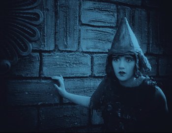 Movie still from “Intolerance” (1916), directed by D.W. Griffith – A woman wearing a pointy hat standing next to a brick wall; Medium shot, High angle