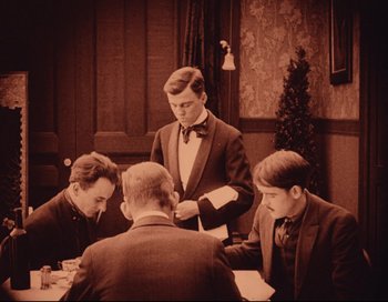 Movie still from “Intolerance” (1916), directed by D.W. Griffith – Three men are sitting at a table and one man is holding a knife; Medium shot, High angle