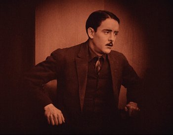 Movie still from “Intolerance” (1916), directed by D.W. Griffith – A man in a suit and tie standing in front of a wall; Medium shot, Low angle