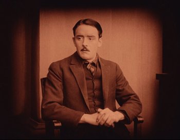 Movie still from “Intolerance” (1916), directed by D.W. Griffith – A man sitting in a chair wearing a suit; Close Up shot, High angle