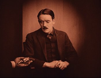 Movie still from “Intolerance” (1916), directed by D.W. Griffith – An old photo of a man in a suit and tie holding a cigarette; Medium shot, High angle
