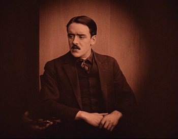 Movie still from “Intolerance” (1916), directed by D.W. Griffith – A man in a suit and tie sitting in a chair; Medium shot, Low angle