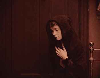 Movie still from “Intolerance” (1916), directed by D.W. Griffith – A young woman in a hooded jacket looking down at her face; Medium shot, High angle