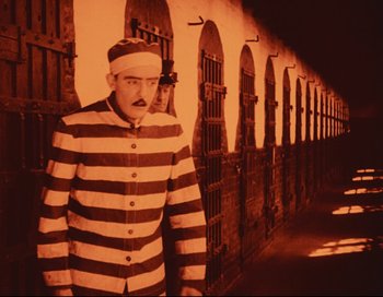 Movie still from “Intolerance” (1916), directed by D.W. Griffith – A man dressed as a prisoner standing in front of a jail cell; Wide shot, Low angle