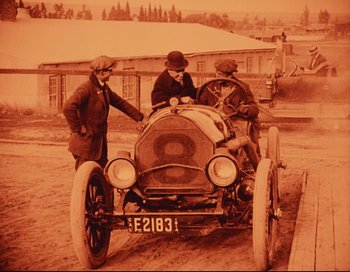 Movie still from “Intolerance” (1916), directed by D.W. Griffith – Three men standing next to an antique car; Wide shot, High angle