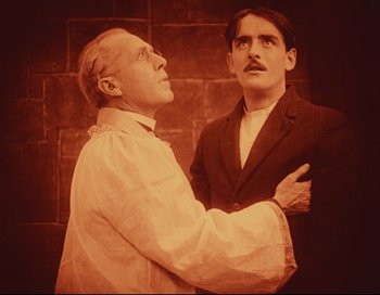 Movie still from “Intolerance” (1916), directed by D.W. Griffith – A man holding another man's arm while standing next to a brick wall; Medium shot, Low angle