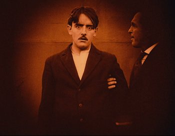 Movie still from “Intolerance” (1916), directed by D.W. Griffith – A man in a suit standing next to another man in a suit; Medium shot, Low angle