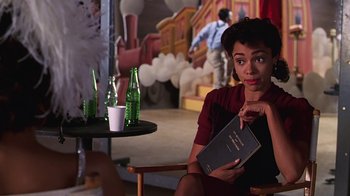 Movie still from “Introducing Dorothy Dandridge” (1999), directed by Martha Coolidge – A woman sitting in front of a table holding a book; Medium shot, Over the shoulder angle