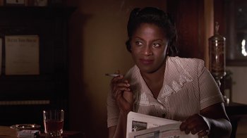 Movie still from “Introducing Dorothy Dandridge” (1999), directed by Martha Coolidge – A woman sitting at a table smoking a cigarette and reading a newspaper; Close Up shot, Over the shoulder angle