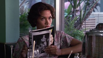 Movie still from “Introducing Dorothy Dandridge” (1999), directed by Martha Coolidge – A woman sitting in front of a window holding a magazine; Close Up shot, Over the shoulder angle
