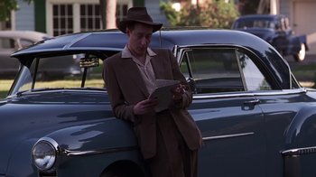 Movie still from “Introducing Dorothy Dandridge” (1999), directed by Martha Coolidge – A man in a suit and hat standing next to a car; Medium shot, Low angle