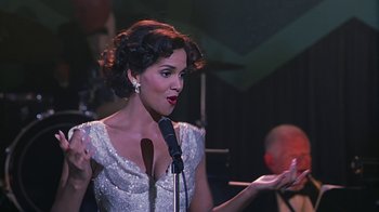 Movie still from “Introducing Dorothy Dandridge” (1999), directed by Martha Coolidge – A woman in a white dress is holding a microphone; Medium shot, Over the shoulder angle