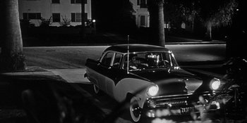 Movie still from “Invasion of the Body Snatchers” (1956), directed by Don Siegel – An old black and white photo of a car on the street; Wide shot, Over the shoulder angle