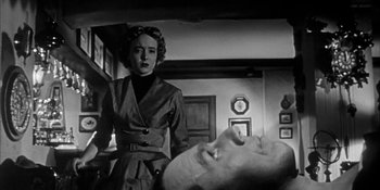 Movie still from “Invasion of the Body Snatchers” (1956), directed by Don Siegel – A black and white photo of a woman standing next to a man's face; Medium shot, Low angle