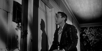 Movie still from “Invasion of the Body Snatchers” (1956), directed by Don Siegel – A black and white photo of a man standing in front of a wall; Medium shot, Low angle