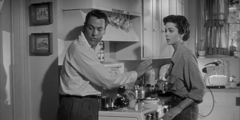 Movie still from “Invasion of the Body Snatchers” (1956), directed by Don Siegel – A man and a woman in the kitchen preparing a meal; Medium shot, Low angle