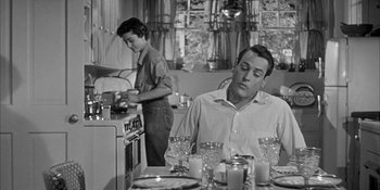 Movie still from “Invasion of the Body Snatchers” (1956), directed by Don Siegel – A man sitting at a table in front of a woman in a kitchen; Medium shot, Low angle