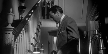 Movie still from “Invasion of the Body Snatchers” (1956), directed by Don Siegel – A black and white photo of a man standing in front of a staircase; Medium shot, Low angle