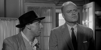 Movie still from “Invasion of the Body Snatchers” (1956), directed by Don Siegel – Two men in suits and hats are standing next to each other in front of a window; Close Up shot, Over the shoulder angle