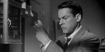 Movie still from “Invasion of the Body Snatchers” (1956), directed by Don Siegel – A black and white photo of a man looking at a cell phone; Close Up shot, Low angle