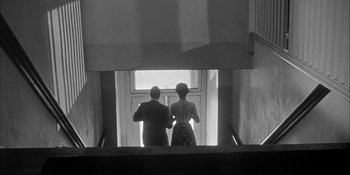 Movie still from “Invasion of the Body Snatchers” (1956), directed by Don Siegel – A man and a woman standing at the bottom of an escalator; Wide shot, Low angle