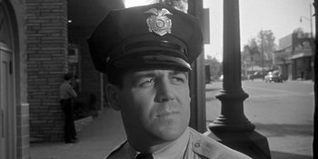 Movie still from “Invasion of the Body Snatchers” (1956), directed by Don Siegel – A man in a police uniform is looking at the camera; Close Up shot, Low angle