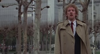Movie still from “Invasion of the Body Snatchers” (1978), directed by Philip Kaufman – A man in a trench coat and a red tie standing in front of trees; Medium shot, Low angle