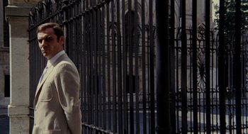 Movie still from “Investigation of a Citizen Above Suspicion” (1970), directed by Elio Petri – A man standing next to an iron fence; Medium shot, Low angle