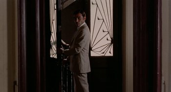 Movie still from “Investigation of a Citizen Above Suspicion” (1970), directed by Elio Petri – A man in a suit standing in front of an open door; Medium shot, Low angle