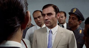 Movie still from “Investigation of a Citizen Above Suspicion” (1970), directed by Elio Petri – A group of men standing next to each other in a room; Close Up shot, Over the shoulder angle