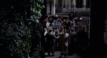 Movie still from “Investigation of a Citizen Above Suspicion” (1970), directed by Elio Petri – A group of people standing around each other in front of a building; Extreme Wide shot, High angle