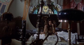 Movie still from “Investigation of a Citizen Above Suspicion” (1970), directed by Elio Petri – A woman sitting on top of a bed next to a stained glass window; Wide shot, High angle