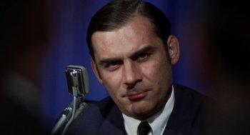 Movie still from “Investigation of a Citizen Above Suspicion” (1970), directed by Elio Petri – A man that is sitting in front of a microphone; Close Up shot, High angle