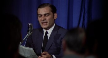 Movie still from “Investigation of a Citizen Above Suspicion” (1970), directed by Elio Petri – A man wearing a suit and tie while holding a microphone; Close Up shot, Low angle