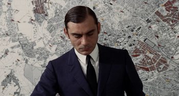 Movie still from “Investigation of a Citizen Above Suspicion” (1970), directed by Elio Petri – A man wearing a suit and tie standing in front of a wall; Close Up shot, High angle
