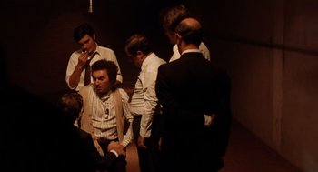 Movie still from “Investigation of a Citizen Above Suspicion” (1970), directed by Elio Petri – A group of men standing around each other in a room; Wide shot, High angle