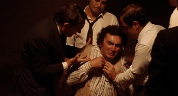 Movie still from “Investigation of a Citizen Above Suspicion” (1970), directed by Elio Petri – A group of men standing around a man in a suit; Medium shot, High angle