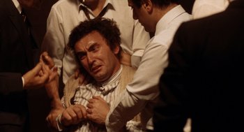 Movie still from “Investigation of a Citizen Above Suspicion” (1970), directed by Elio Petri – A group of men standing around a man with his hands on his chest; Close Up shot, Overhead angle