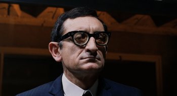 Movie still from “Investigation of a Citizen Above Suspicion” (1970), directed by Elio Petri – An older man wearing glasses and a suit; Close Up shot, Low angle