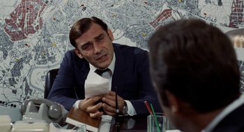 Movie still from “Investigation of a Citizen Above Suspicion” (1970), directed by Elio Petri – A man sitting at a table holding a piece of paper; Close Up shot, Over the shoulder angle