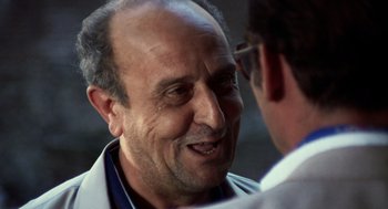 Movie still from “Investigation of a Citizen Above Suspicion” (1970), directed by Elio Petri – An older man is smiling while looking at a younger man; Close Up shot, Over the shoulder angle