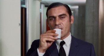 Movie still from “Investigation of a Citizen Above Suspicion” (1970), directed by Elio Petri – A man wearing a suit and tie drinking a cup of coffee; Close Up shot, Low angle