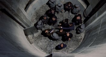 Movie still from “Investigation of a Citizen Above Suspicion” (1970), directed by Elio Petri – A group of men standing around in a circle; Extreme Wide shot, Overhead angle