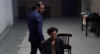 Movie still from “Investigation of a Citizen Above Suspicion” (1970), directed by Elio Petri – A man in a blue suit standing next to another man in a brown shirt; Medium shot, High angle