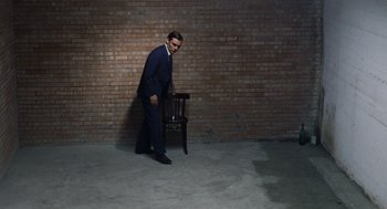 Movie still from “Investigation of a Citizen Above Suspicion” (1970), directed by Elio Petri – A man standing next to a chair in a room; Wide shot, High angle