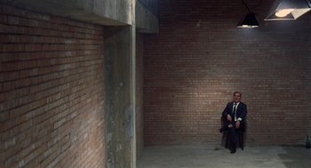 Movie still from “Investigation of a Citizen Above Suspicion” (1970), directed by Elio Petri – A man in a suit and tie sitting on a bench; Wide shot, High angle