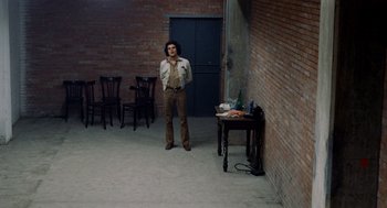 Movie still from “Investigation of a Citizen Above Suspicion” (1970), directed by Elio Petri – A person standing in a room with a table and chairs; Wide shot, High angle