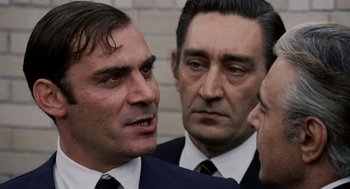 Movie still from “Investigation of a Citizen Above Suspicion” (1970), directed by Elio Petri – A group of men standing next to each other in suits; Close Up shot, Over the shoulder angle